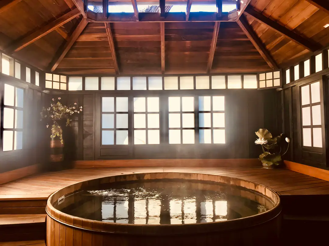 A round wooden soaking tub in a timber bathhouse with tall windows