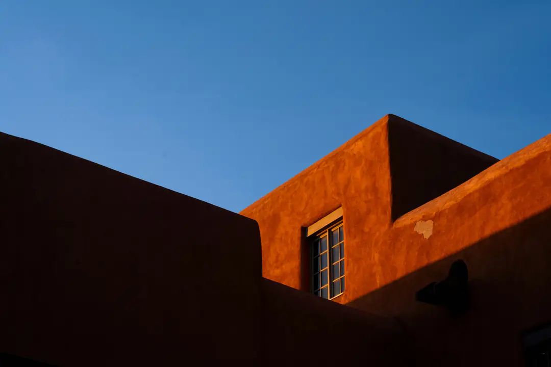 A terracotta-red adobe wall and window under a clear blue sky