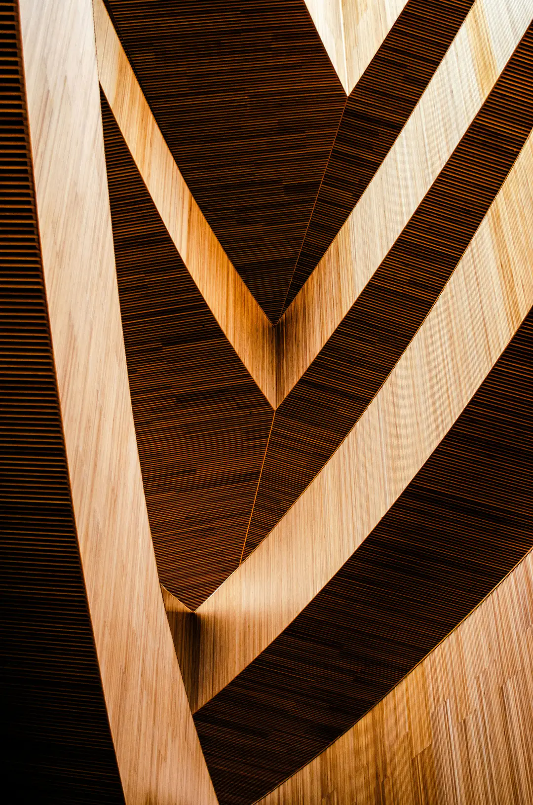 Abstract chevrons of pale and dark timber lit warmly from the side