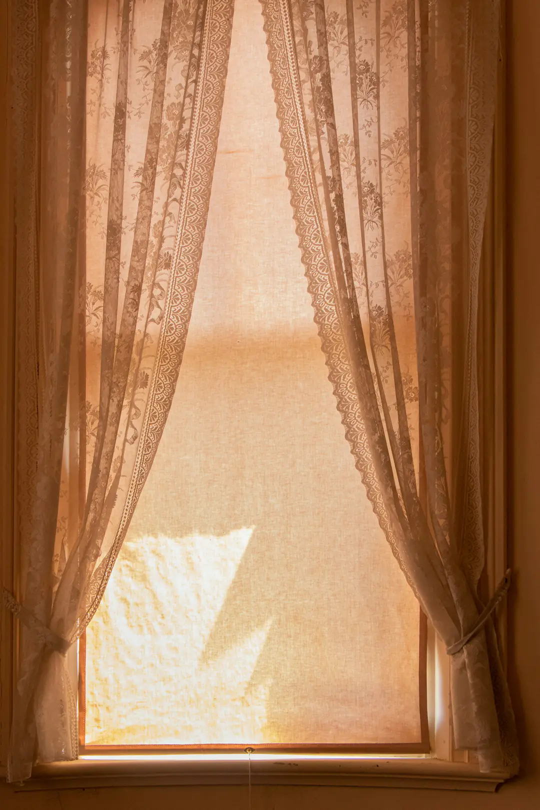Afternoon sun glowing through sheer amber curtains at a tall window