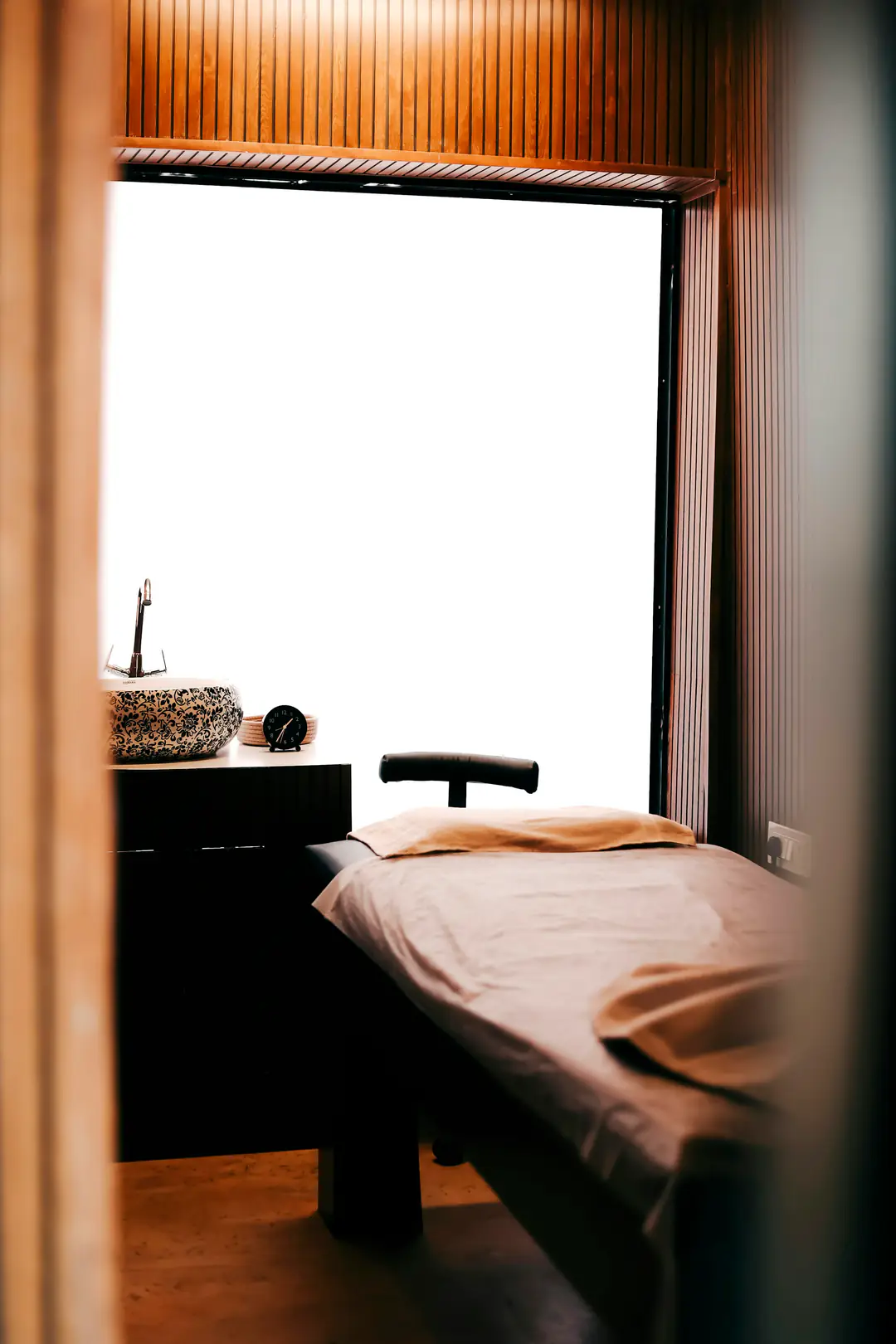 A treatment room with a linen-dressed massage table beside a bright window