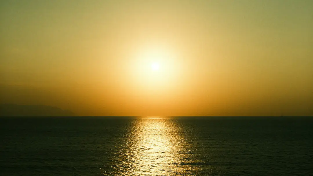 The sun setting into a flat, glassy ocean