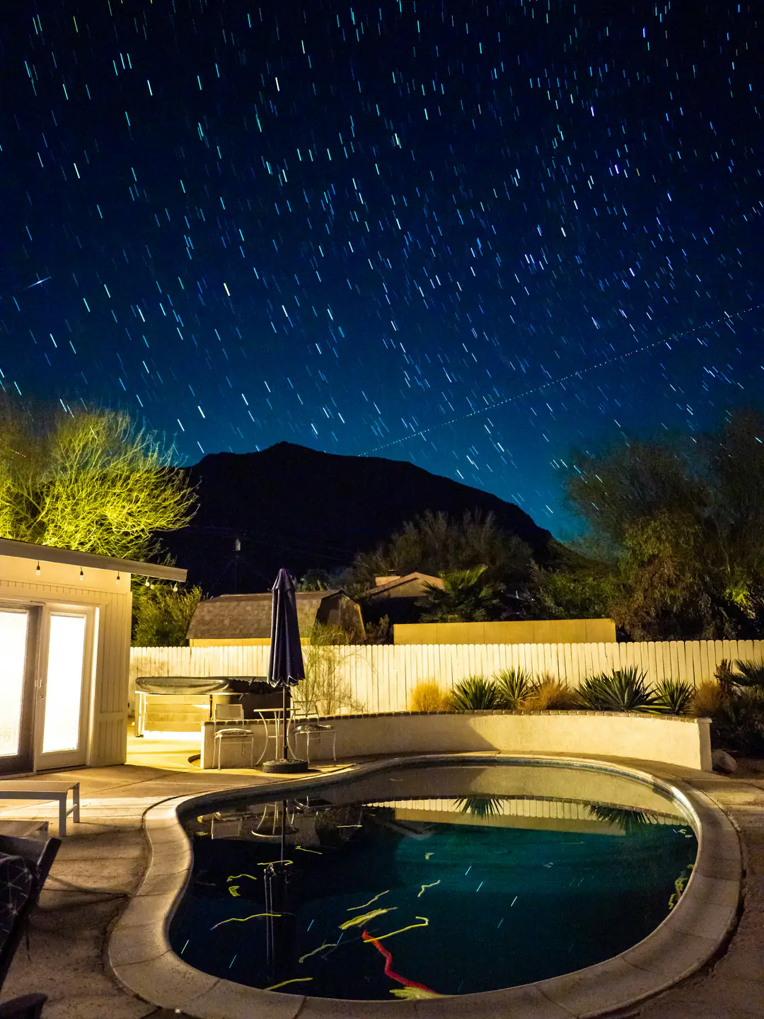 Star trails over a desert mountain and a softly lit pool at night