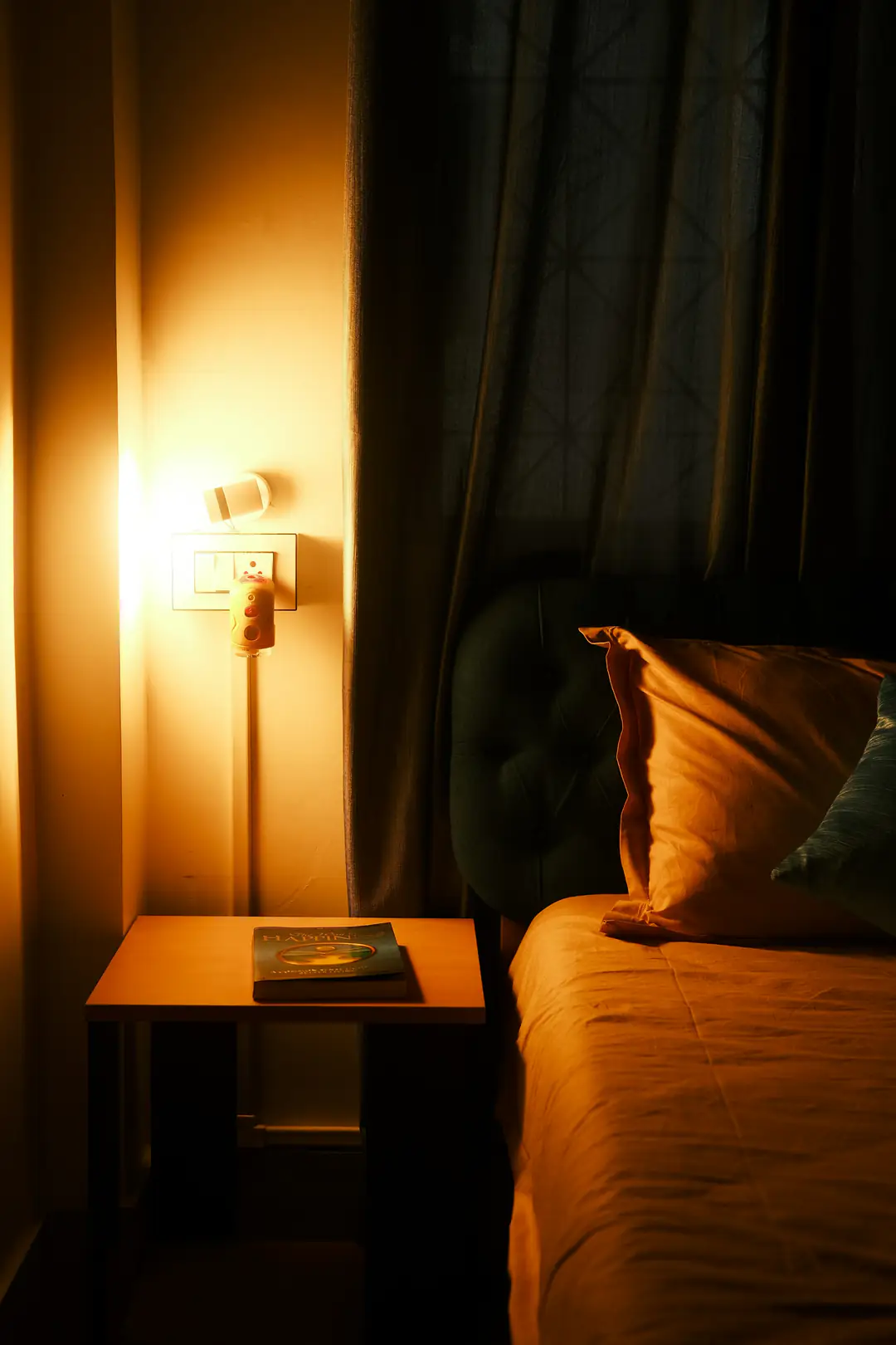 A bedside lamp casting amber light over a dark headboard and folded bedding at night